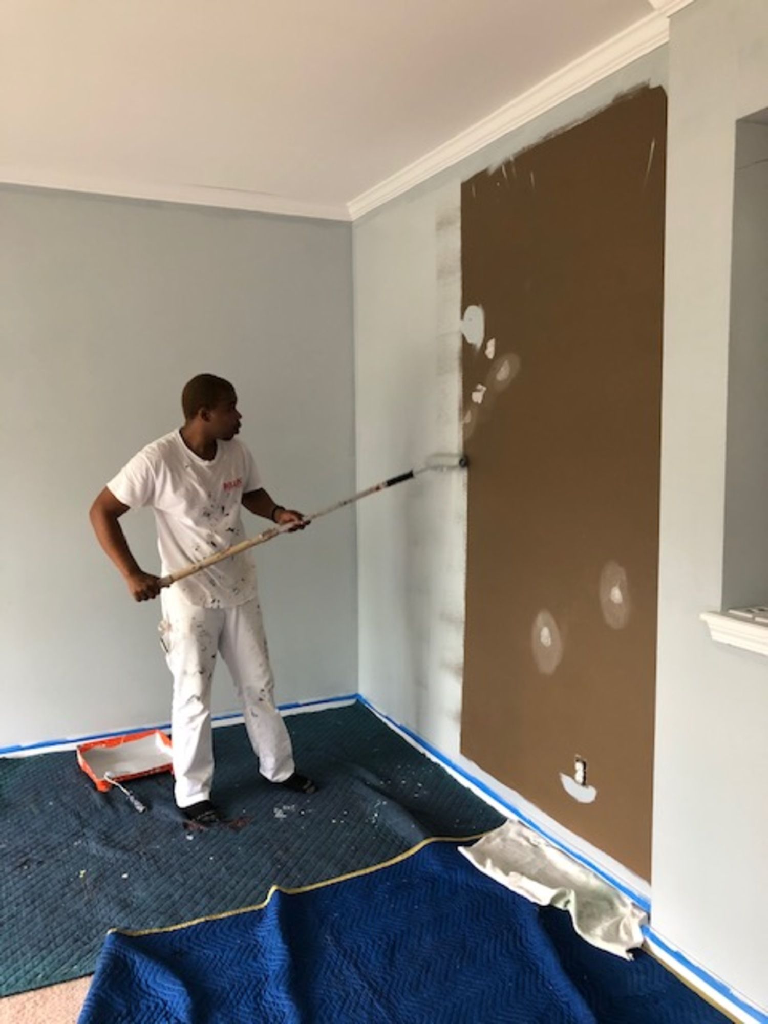 A man is painting a wall with a roller in a room.