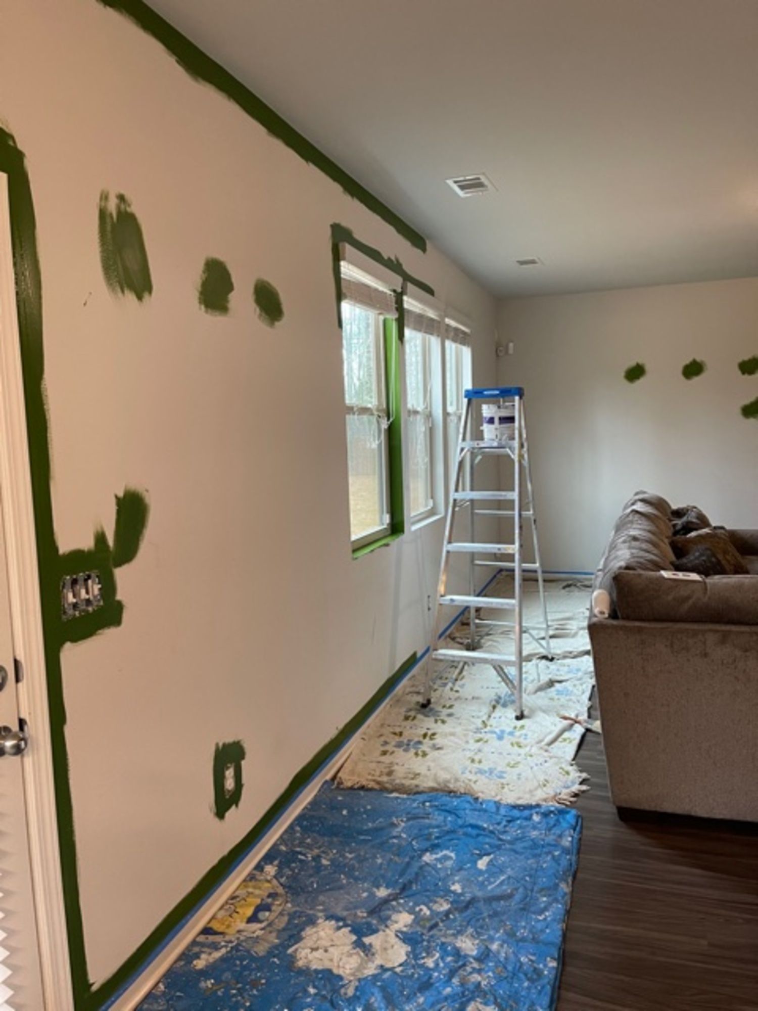 A living room with a ladder and a couch being painted.