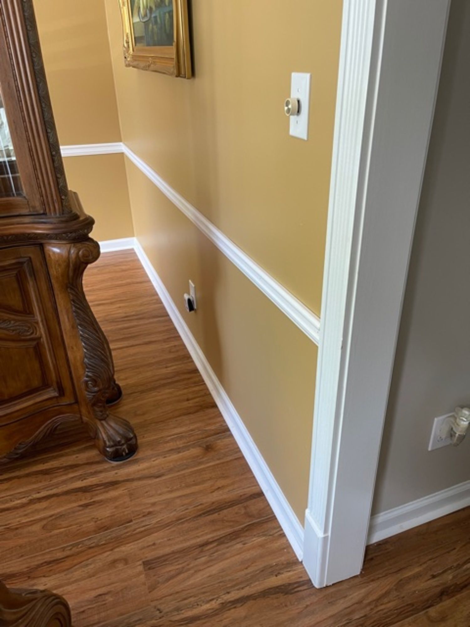 A hallway with hardwood floors , yellow walls and white trim.