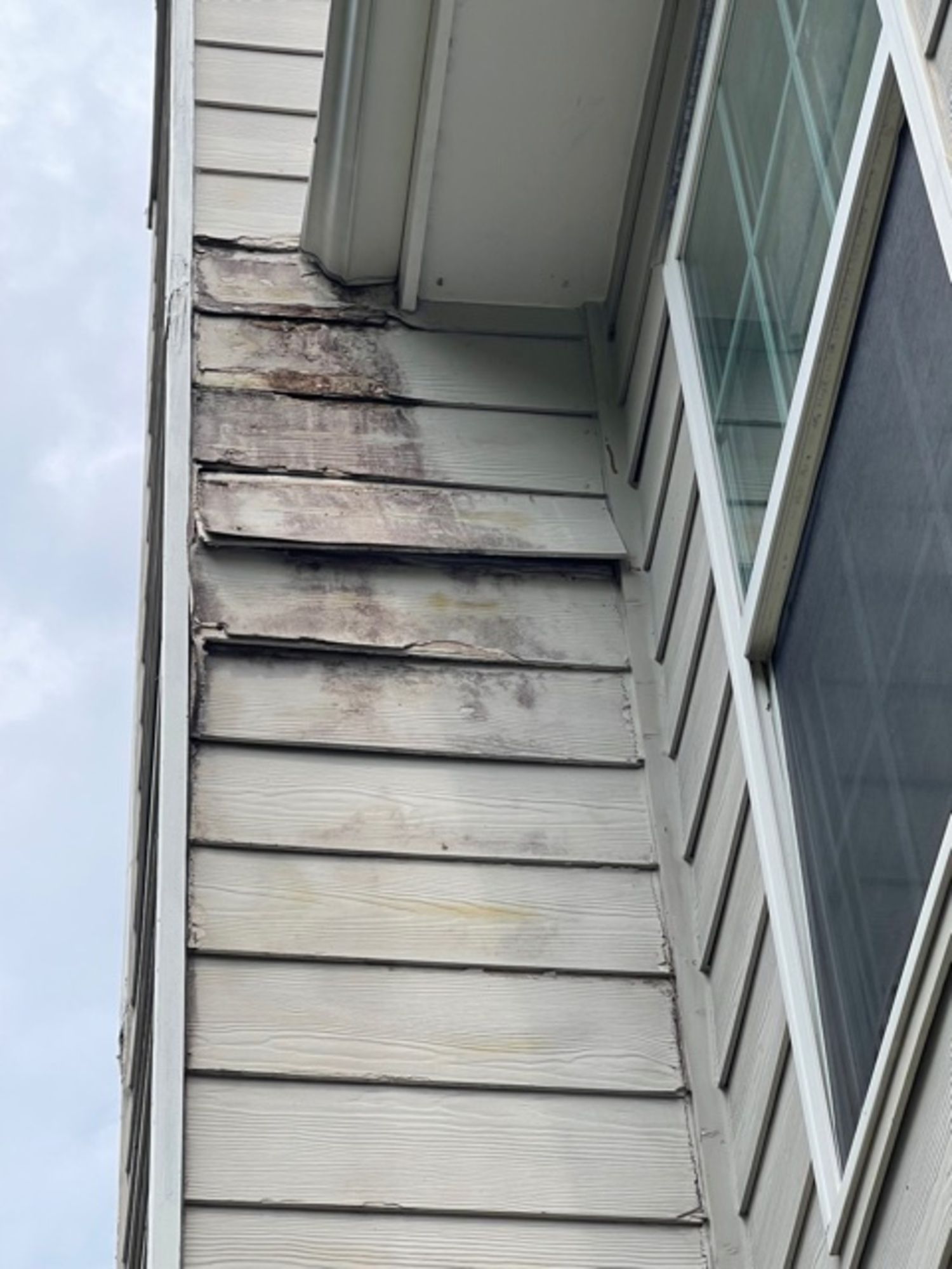 A close up of a house with peeling siding and a window.