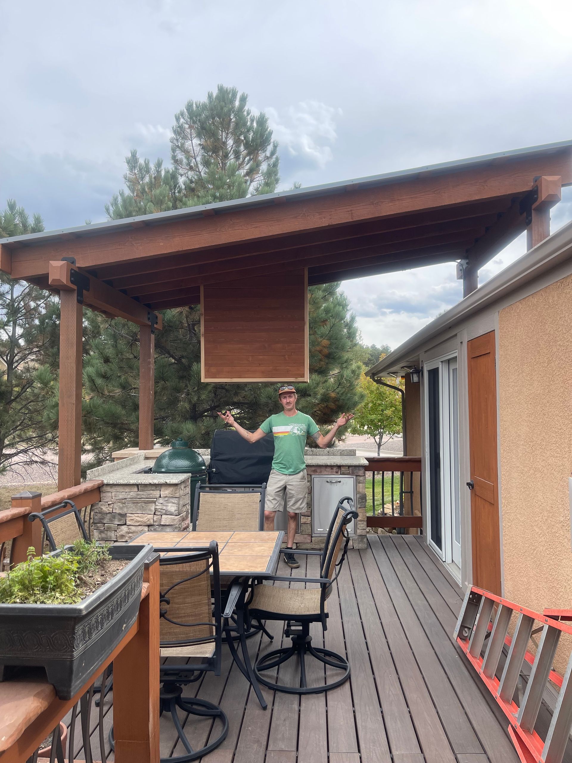A man is standing on a deck with a table and chairs under a canopy.