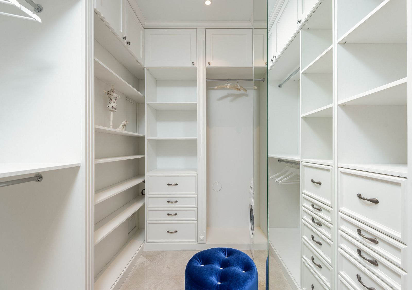 A walk in closet with lots of shelves and drawers and a blue ottoman.