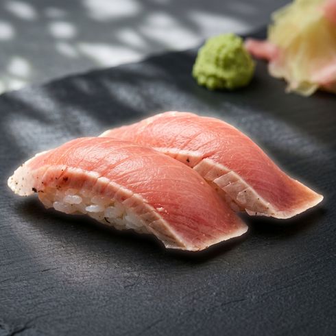 Two pieces of salmon sushi on a black plate with wasabi in the background