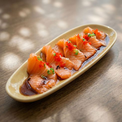 Sliced salmon sashimi on an oval plate, garnished with herbs on a wooden table.