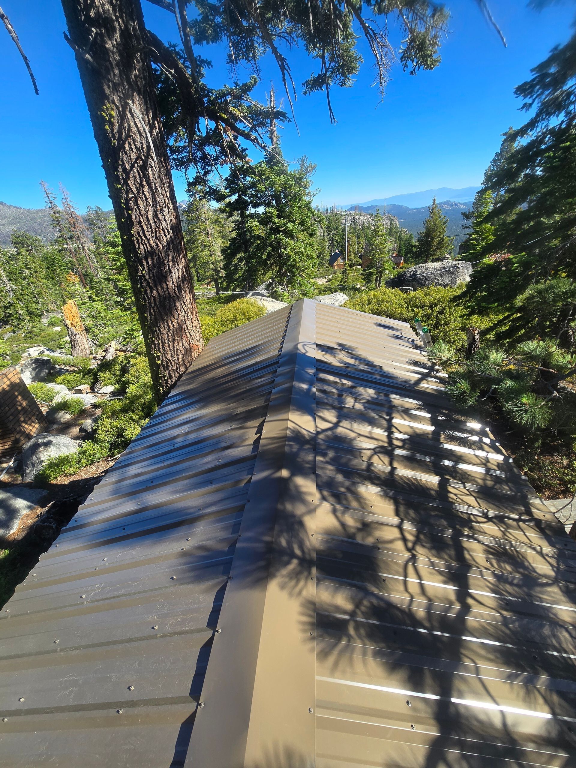 Metal roof ridge between trees with mountain view and blue sky