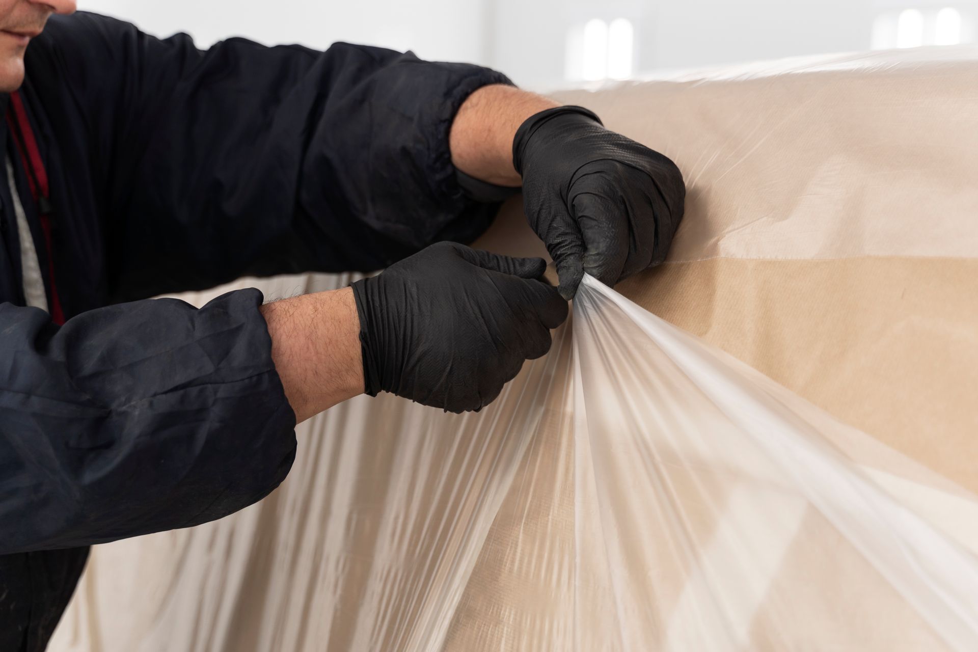 A man wearing black gloves is cutting a piece of plastic.