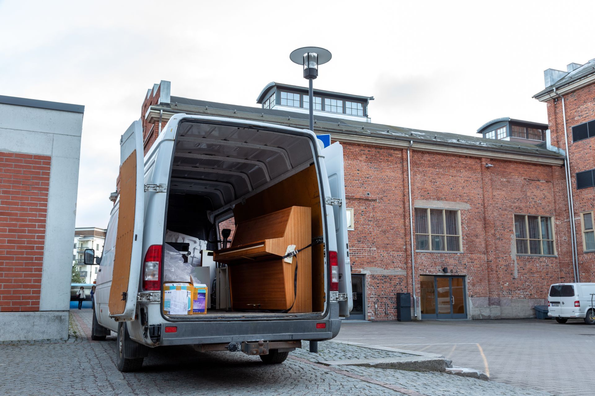 A white van with the back door open is parked in front of a brick building.