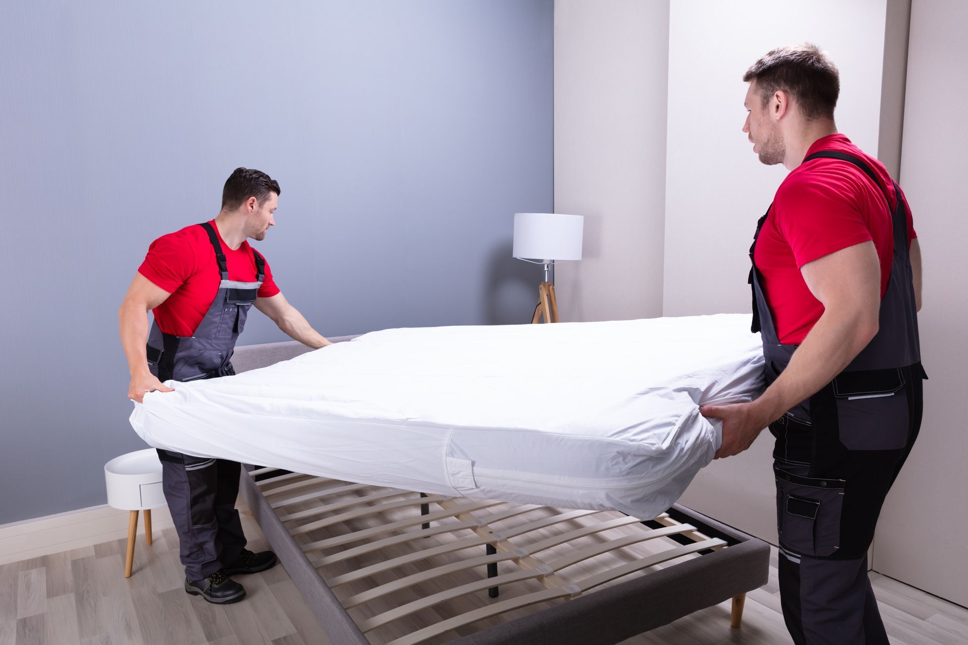 Two men are putting a mattress on a bed in a bedroom.