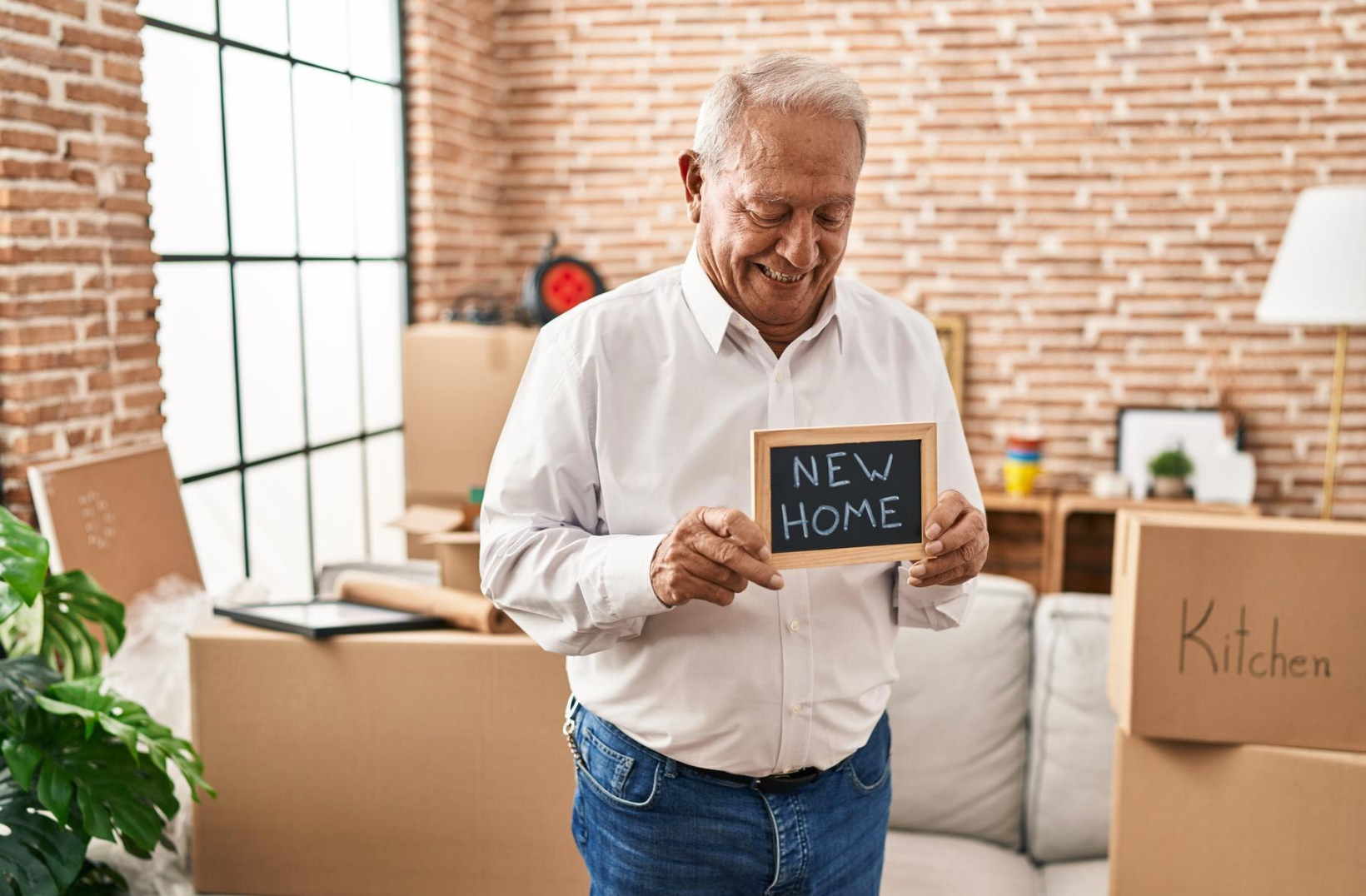 An elderly man is holding a sign that says `` new home '' in a living room.