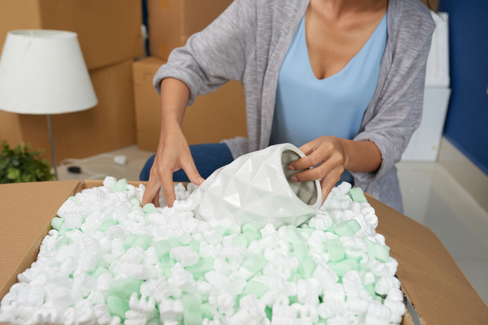 A woman is putting a vase in a cardboard box.