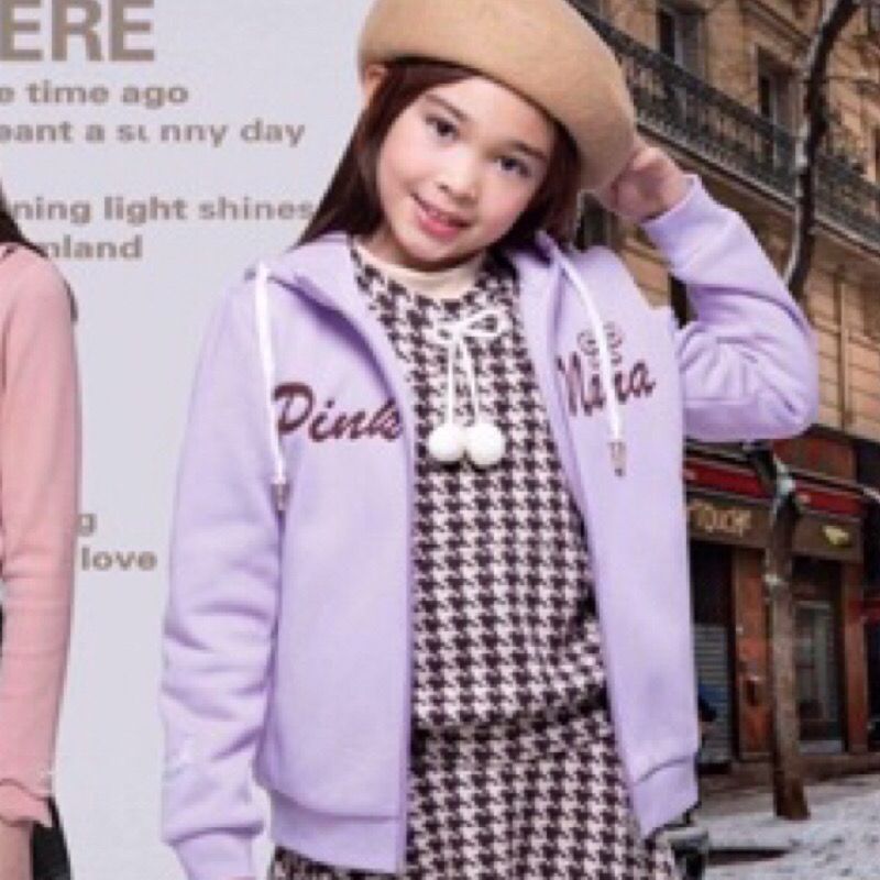 戴著粉紅色無帽沿帽和藍色連帽衫的小女孩微笑著。文字部分可見。