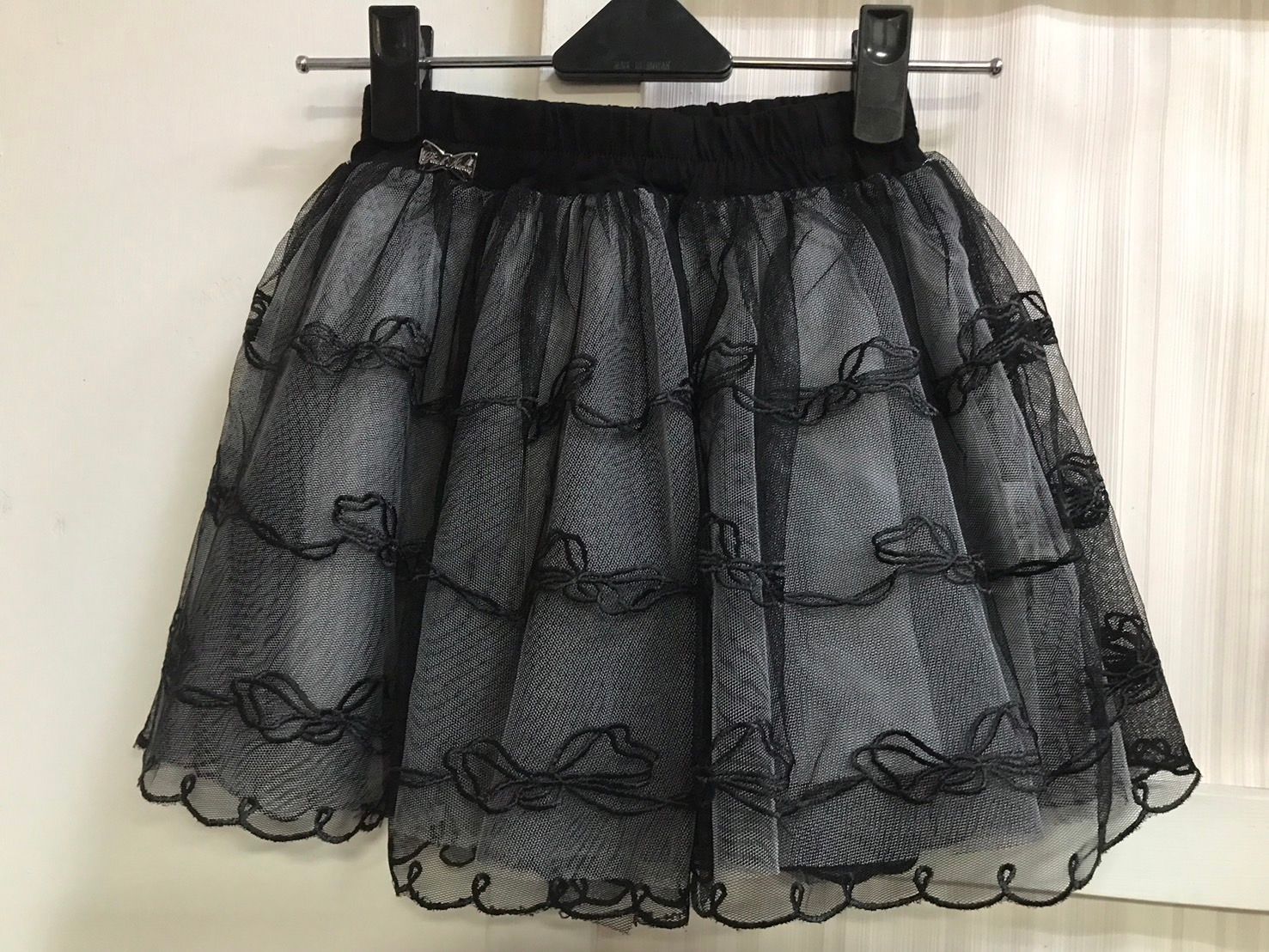 兩個穿著相配裙子的小女孩，一個穿著毛衣背心，另一個穿著紅襯衫，對著鏡頭微笑。