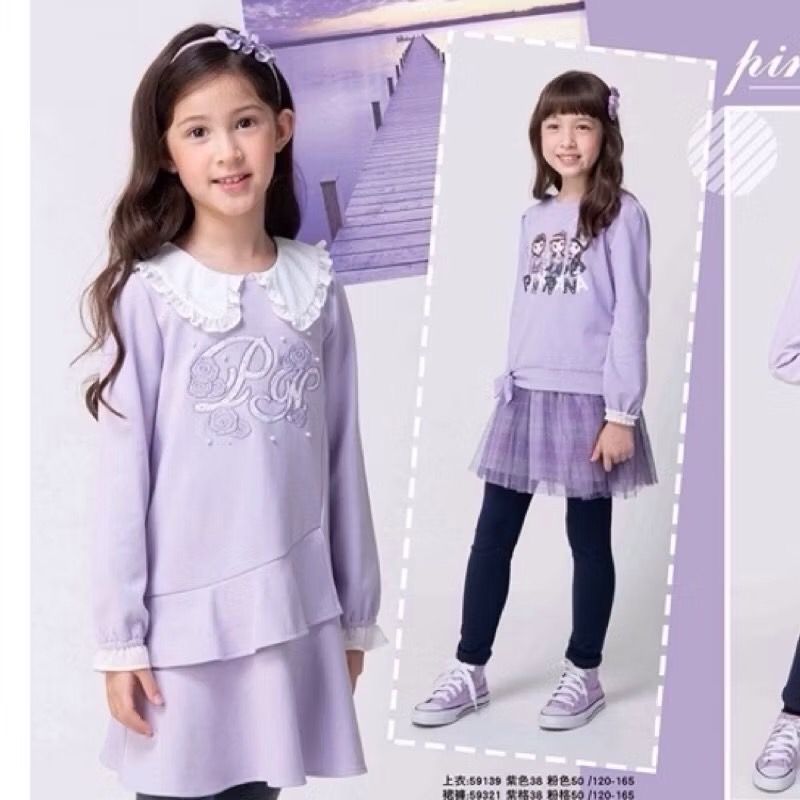 一位身穿粉紅色洋裝、頭戴髮帶的女孩微笑著擺姿勢拍照。白色緊身褲和手提包讓她的造型更加完美。