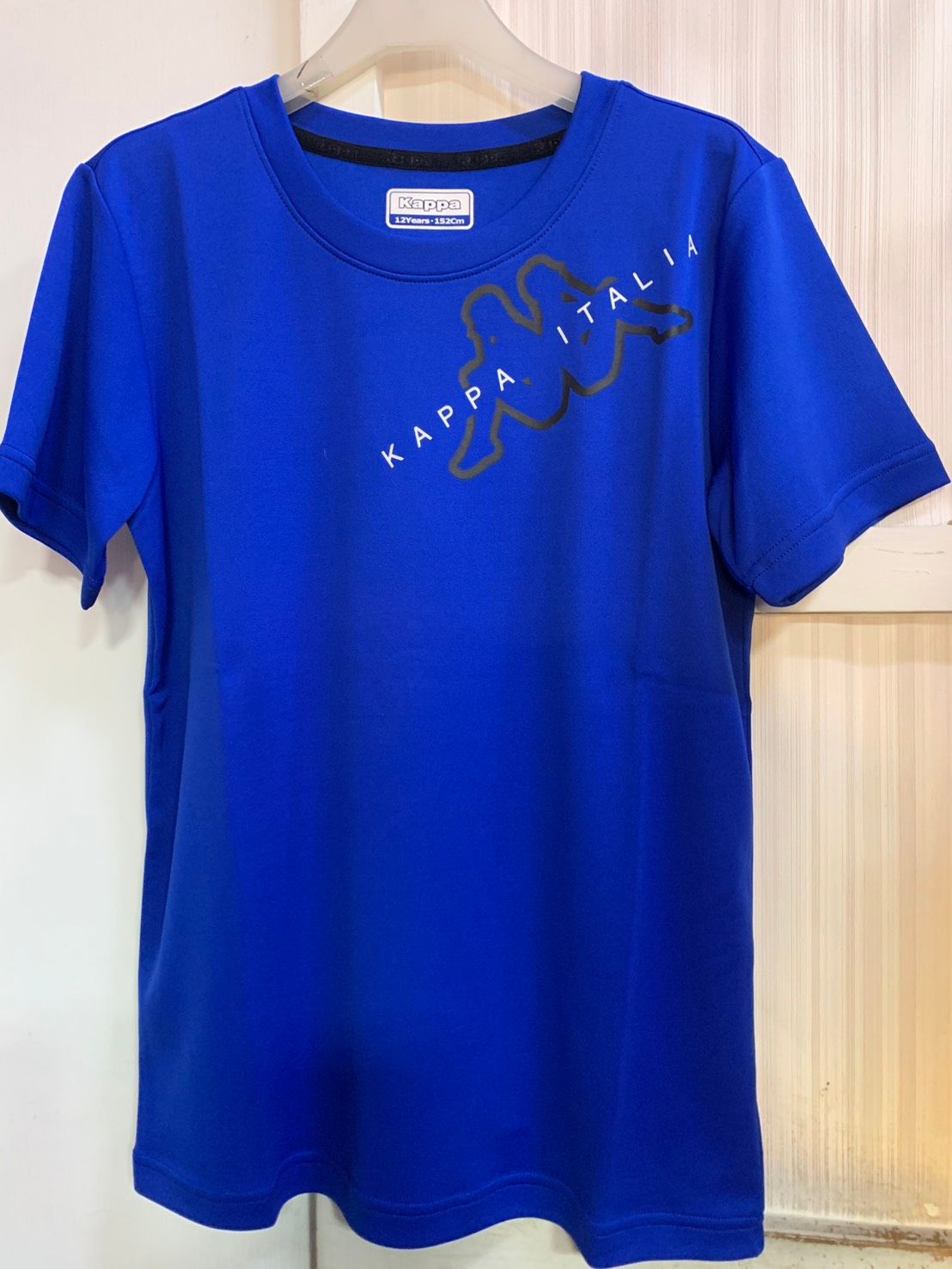 紅色的 Kappa Italia T 卹，帶有黑色標誌和文字，掛在白色牆壁的白色衣架上。