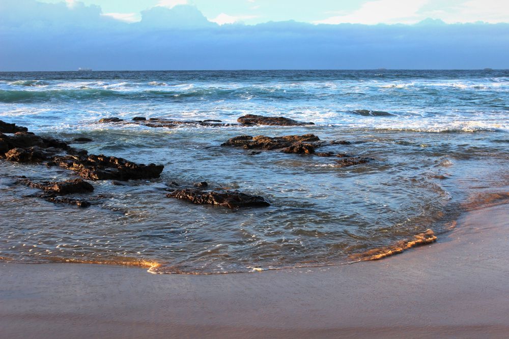 A Beach With Rocks In The Water And Waves Crashing On The Shore — Roof & Guttering Solutions In Saratoga, NSW