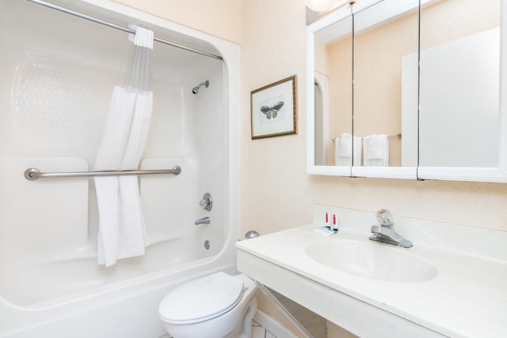 Bathroom with a white tub, toilet, and sink. A framed picture hangs above the toilet.