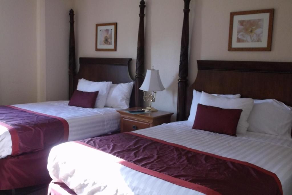 Two beds in a hotel room with dark wood headboards, burgundy accents, and small framed art.
