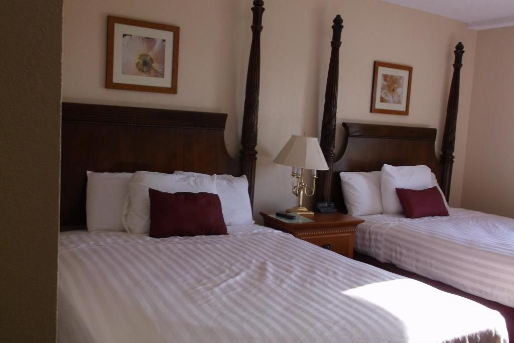 Two beds in a hotel room with dark wood posts, white linens, and burgundy pillows.