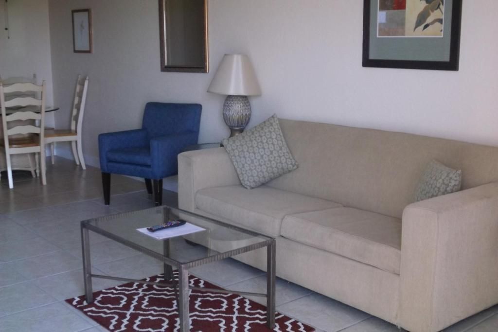 Living room with beige couch, blue armchair, glass coffee table, and dining set.