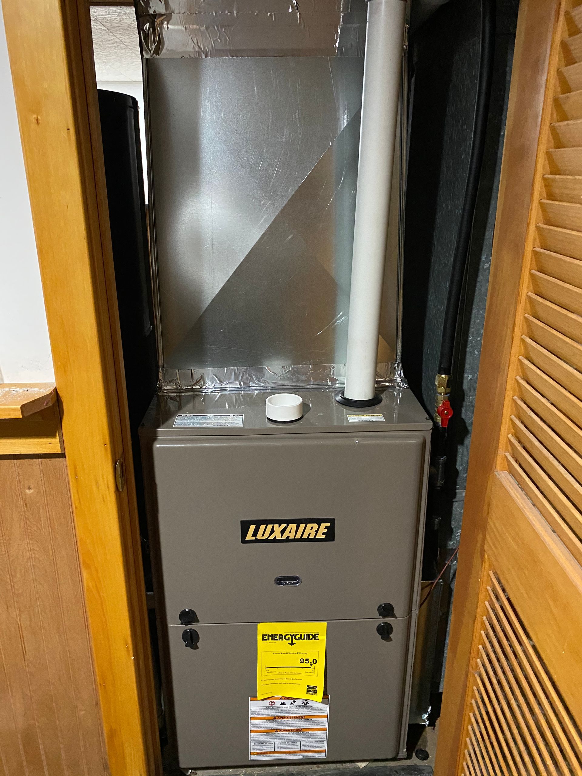 Furnace in closet; gray metal box, white vent pipe, yellow energy efficiency sticker.