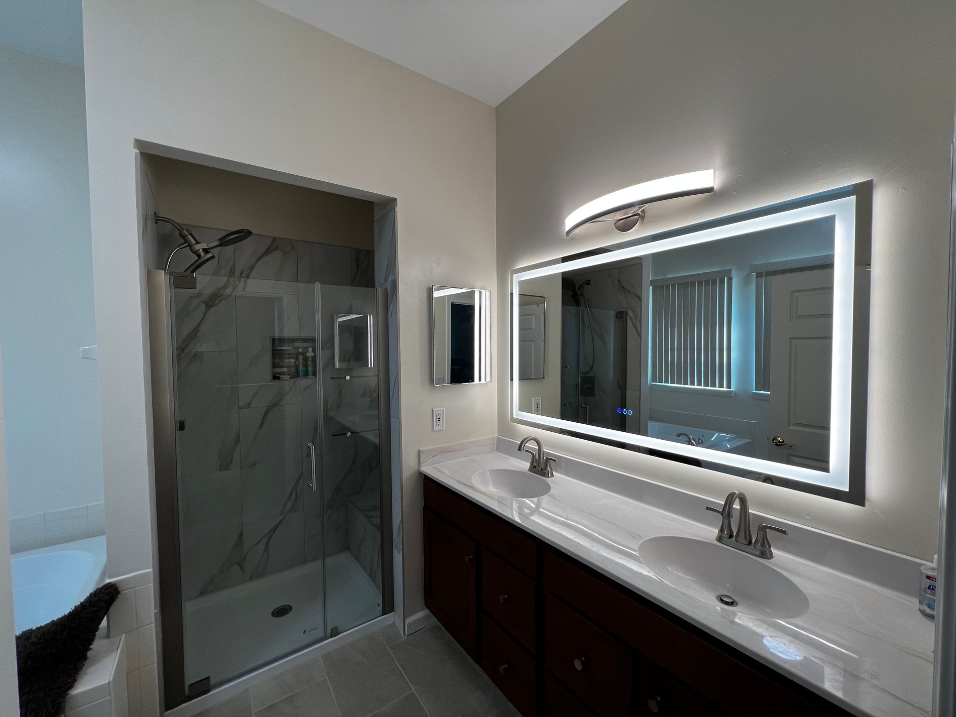 Modern bathroom with a marble shower, double vanity, and lit mirror.