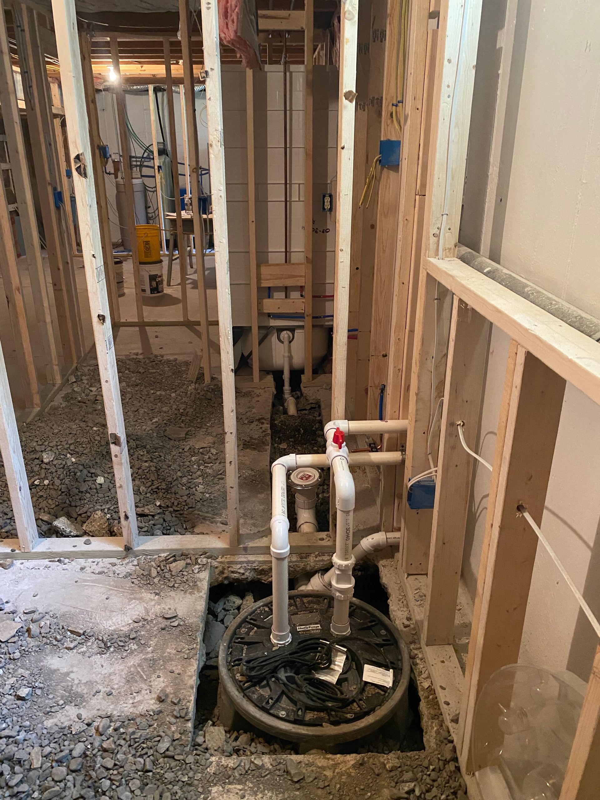 Interior construction site with exposed framing, sump pump, and piping.