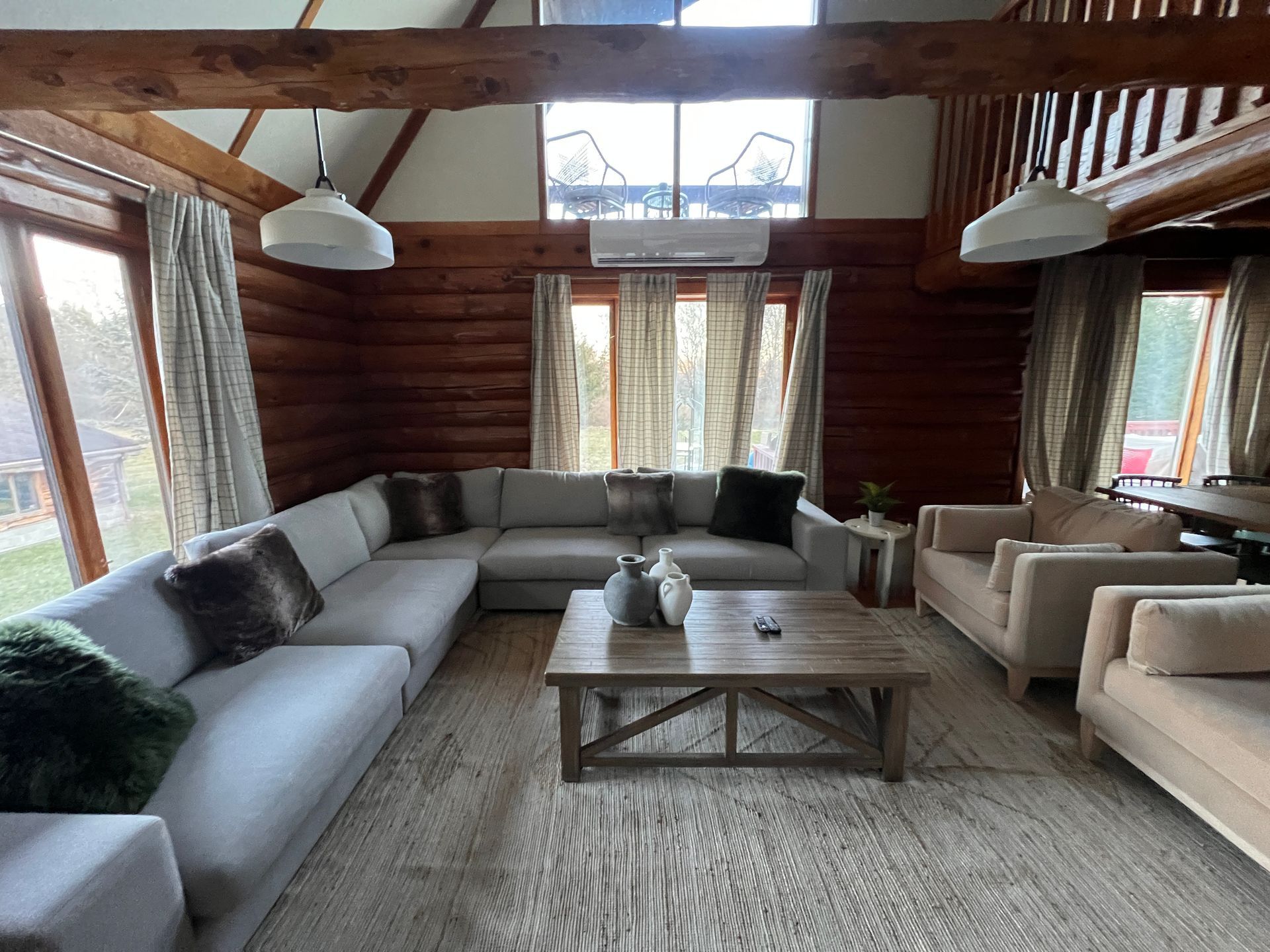 Spacious living room with a large gray sectional, wooden beams, and large windows.