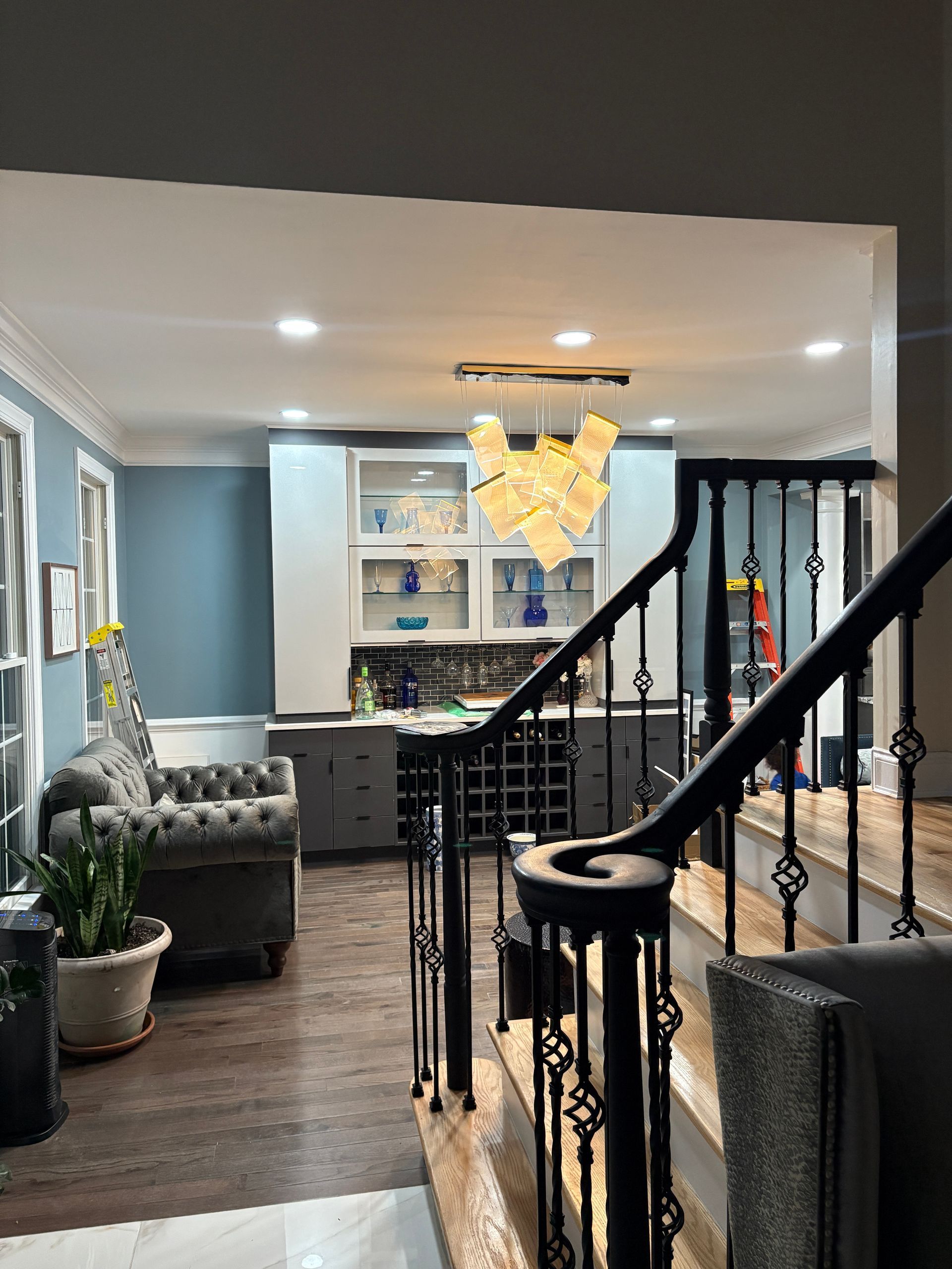 Interior view of a home with a staircase, bar area with cabinets, and a tufted sofa against a blue wall.