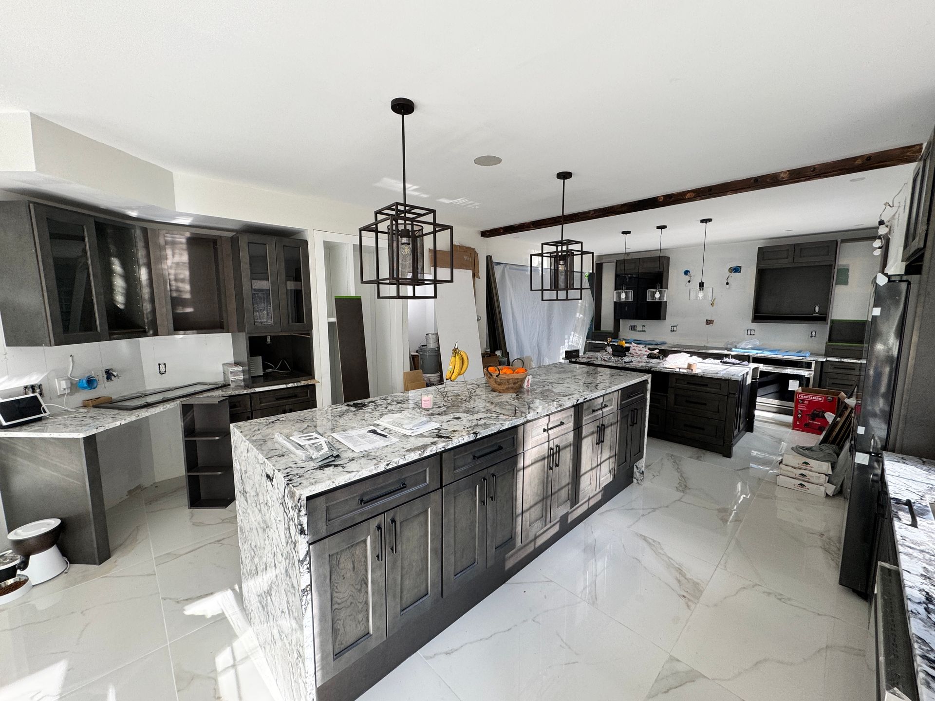 Modern kitchen under construction with gray cabinets, large island, and marble countertops.