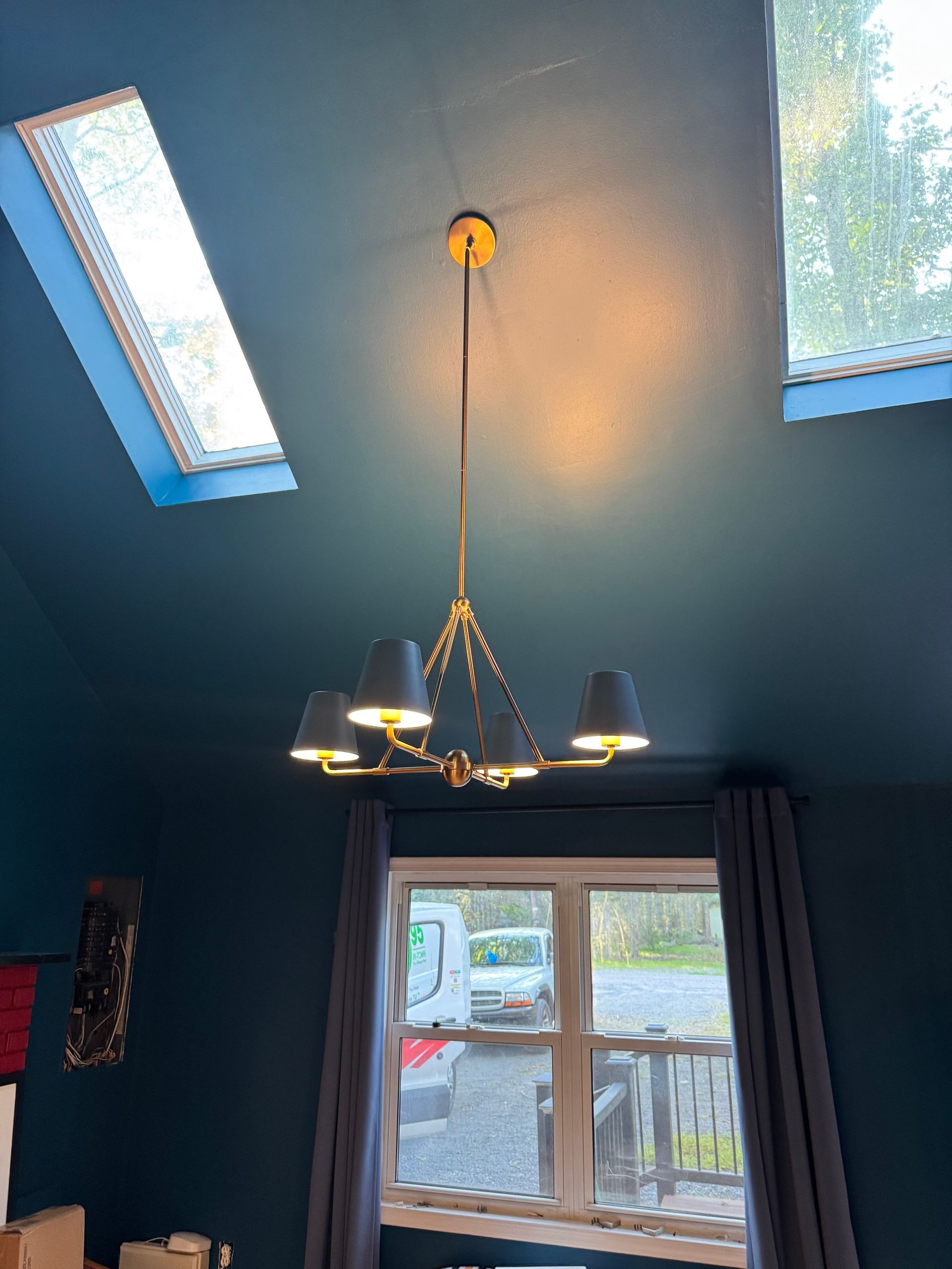 Gold chandelier with black shades hangs from a teal ceiling between skylights.