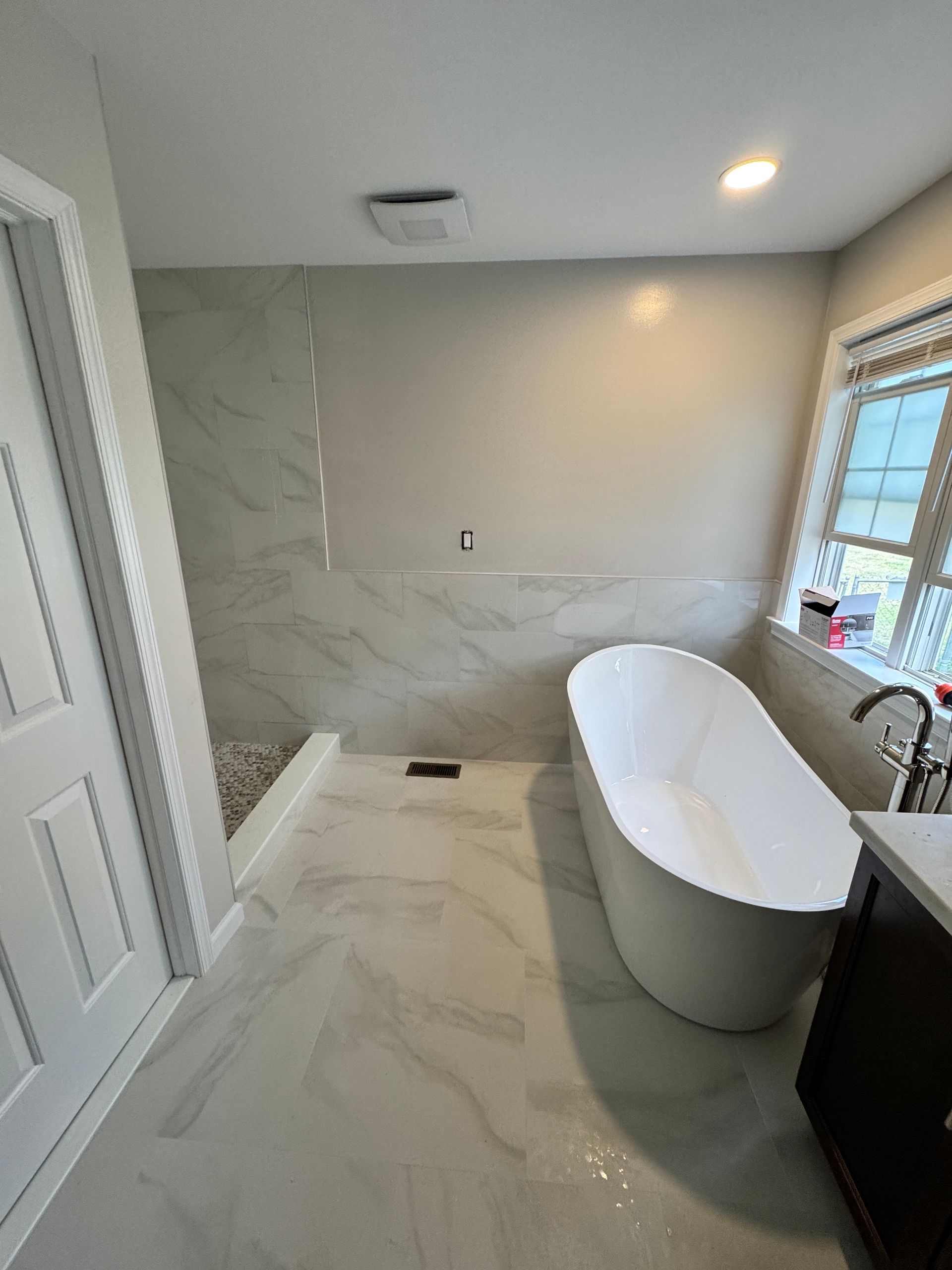 Modern bathroom with a white freestanding bathtub, marble tile, and a shower.