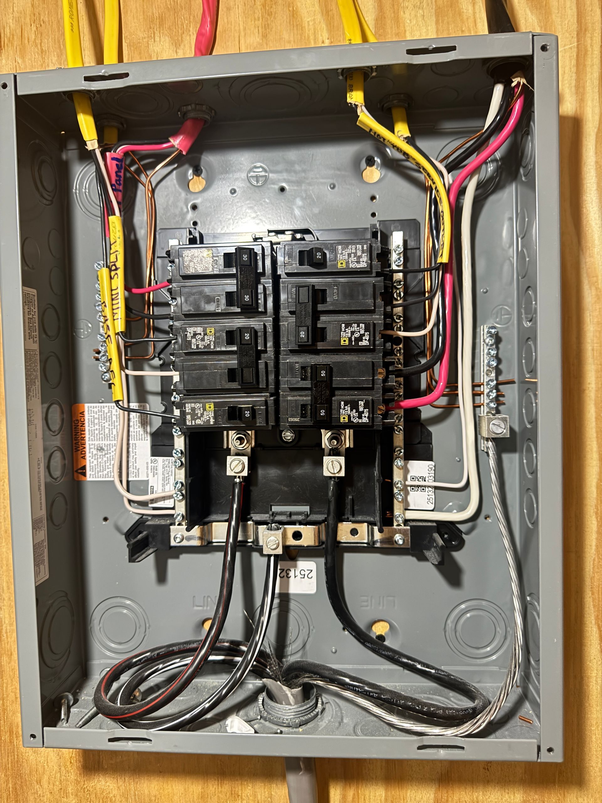 Electrical panel with circuit breakers and wires inside a metal box.