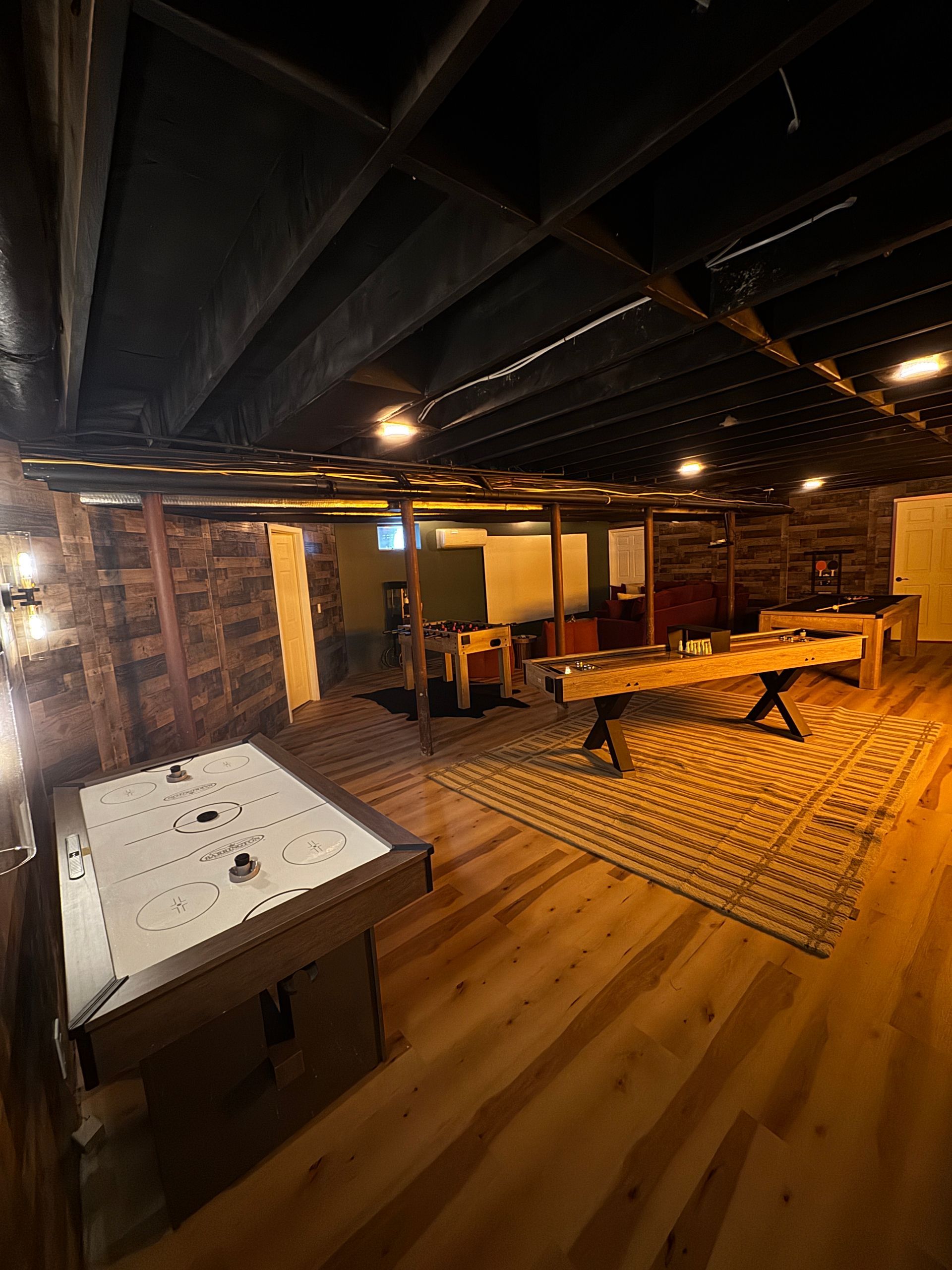 Basement game room with pool and foosball tables, rug, wood floor, and exposed ceiling beams.