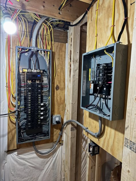 Two electrical panels mounted on plywood walls with various wires and conduits.