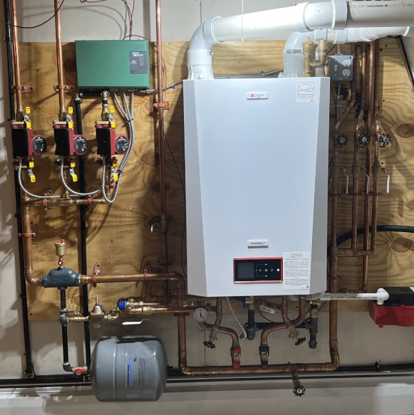 A wall-mounted, white boiler with copper pipes, pumps, and a green control box.
