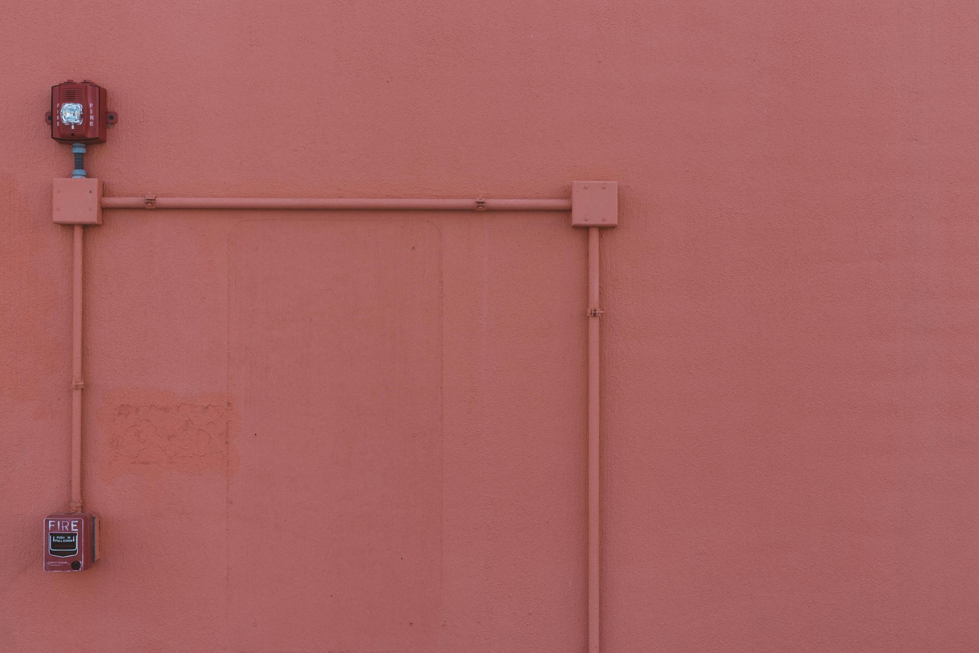Red wall with fire alarm system, pipes, and electrical boxes.