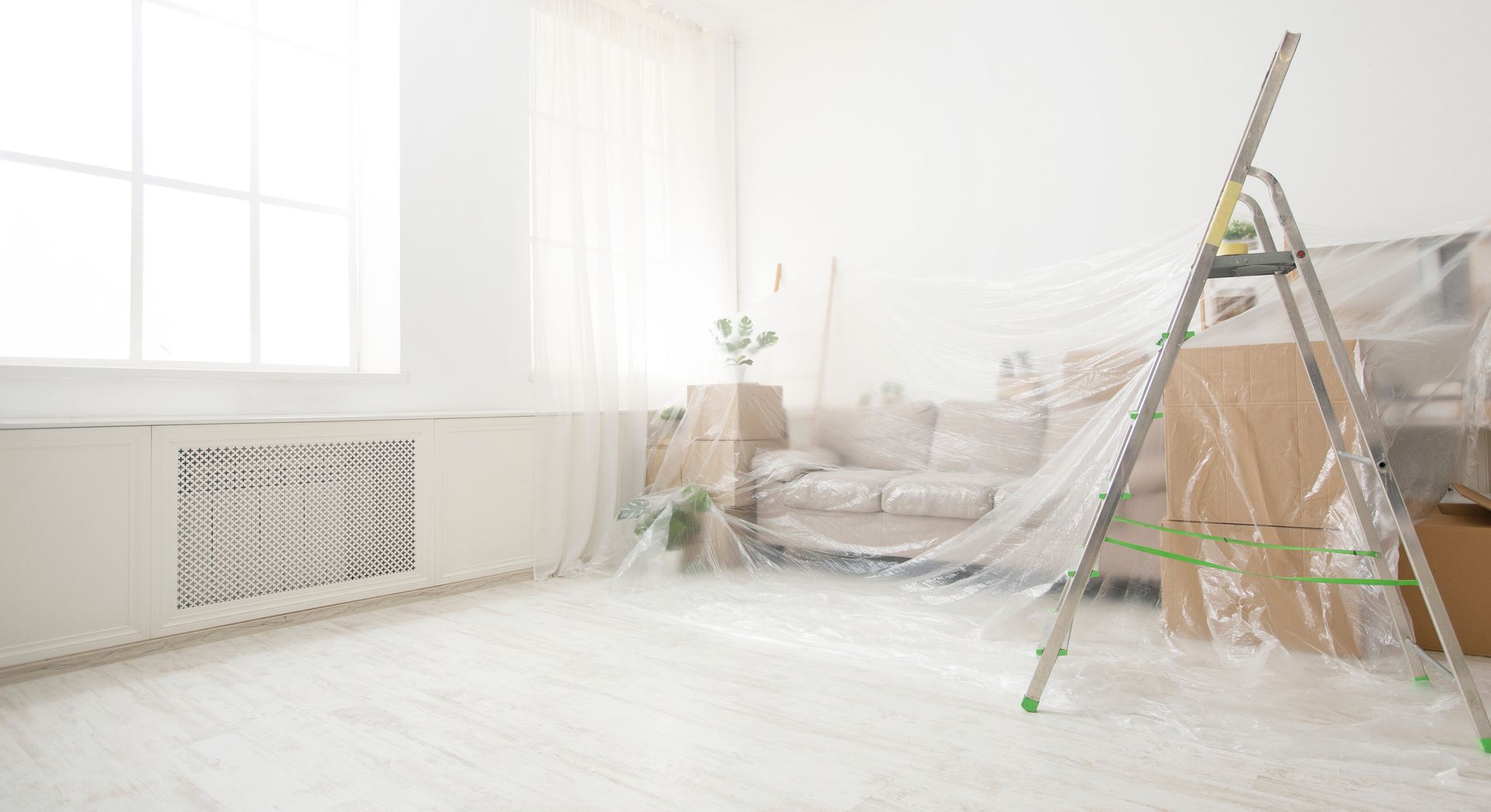 Room being prepared for painting, furniture covered in plastic, stepladder, bright light. Room being prepared for painting, furniture covered in plastic, stepladder, bright light.