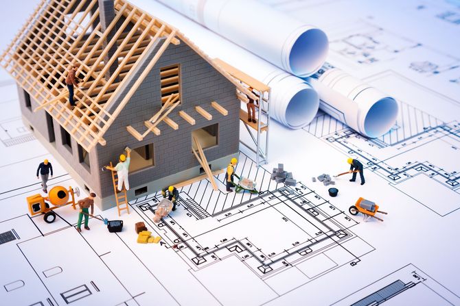 Miniature house under construction on architectural blueprints with tiny figures. Miniature house under construction on architectural blueprints with tiny figures.