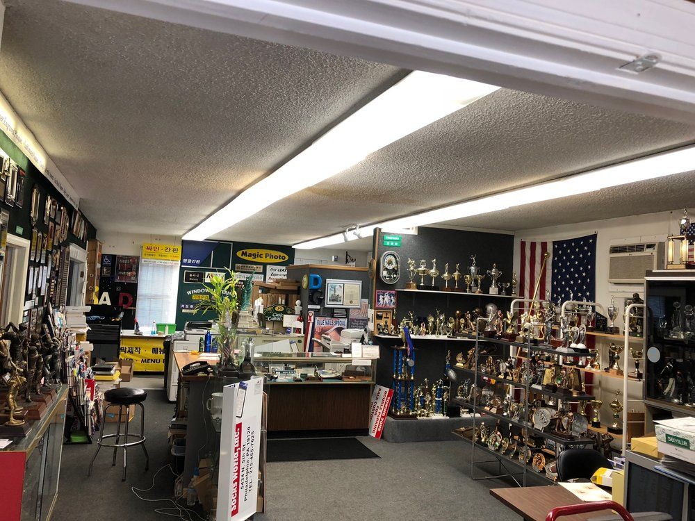 Interior of a trophy shop; shelves and display cases filled with trophies. American flag on the wall.
