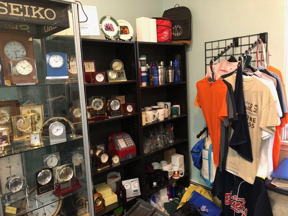 Inside a shop, a display case of clocks and shelves of merchandise including clocks, mugs, and shirts.