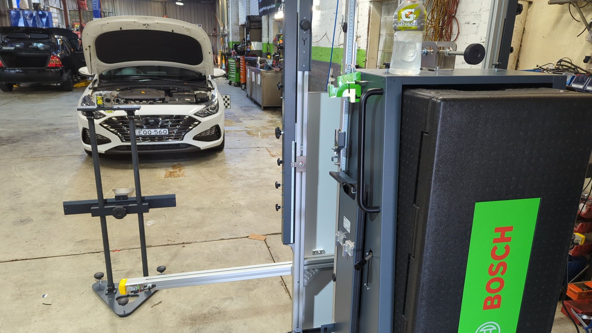 A white car with the hood up is sitting in a garage next to a bosch machine.