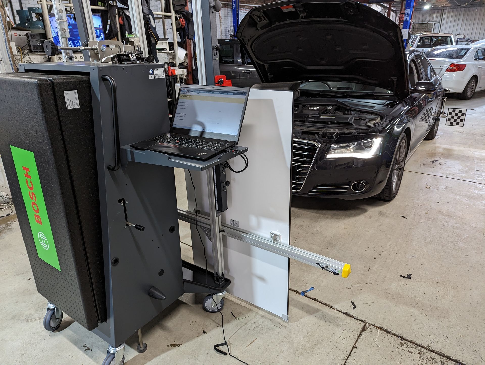 A car with the hood up is being worked on in a garage.