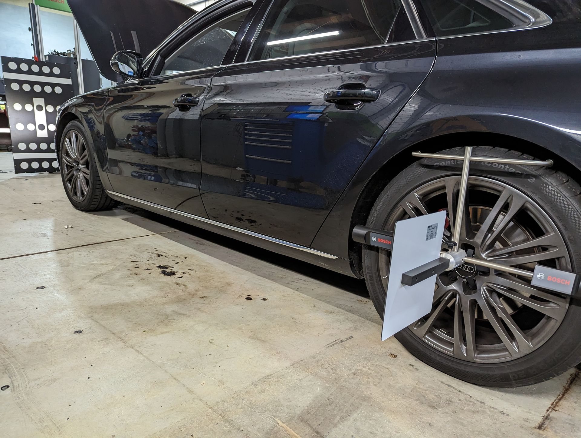 A car is being adjusted in a garage with a wheel alignment machine.