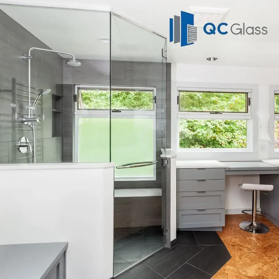 A modern bathroom featuring a glass-enclosed shower, gray cabinetry, and a vanity area with a stool.