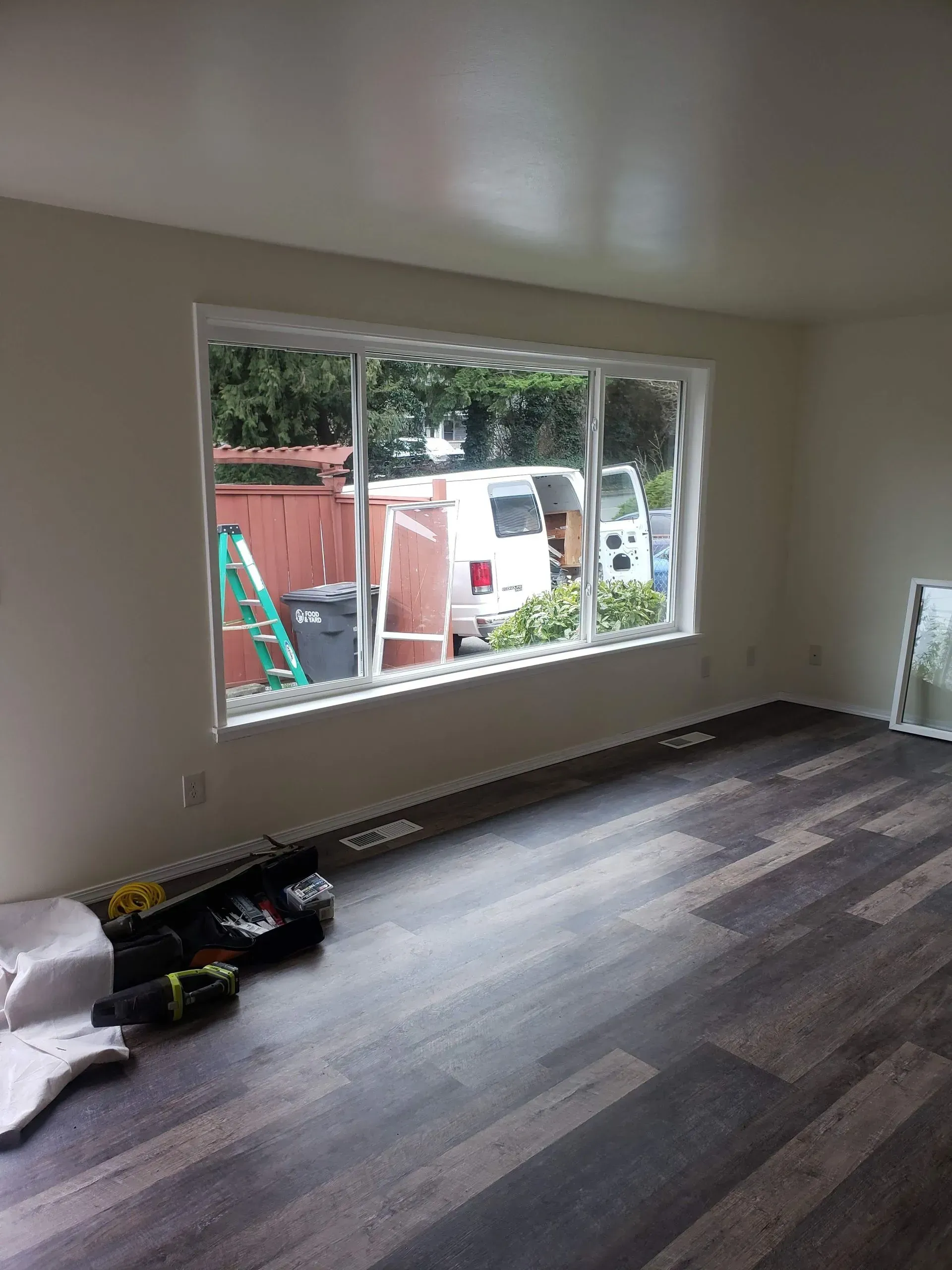 A person digs a trench in a backyard near a small excavator, a tree, and a house.