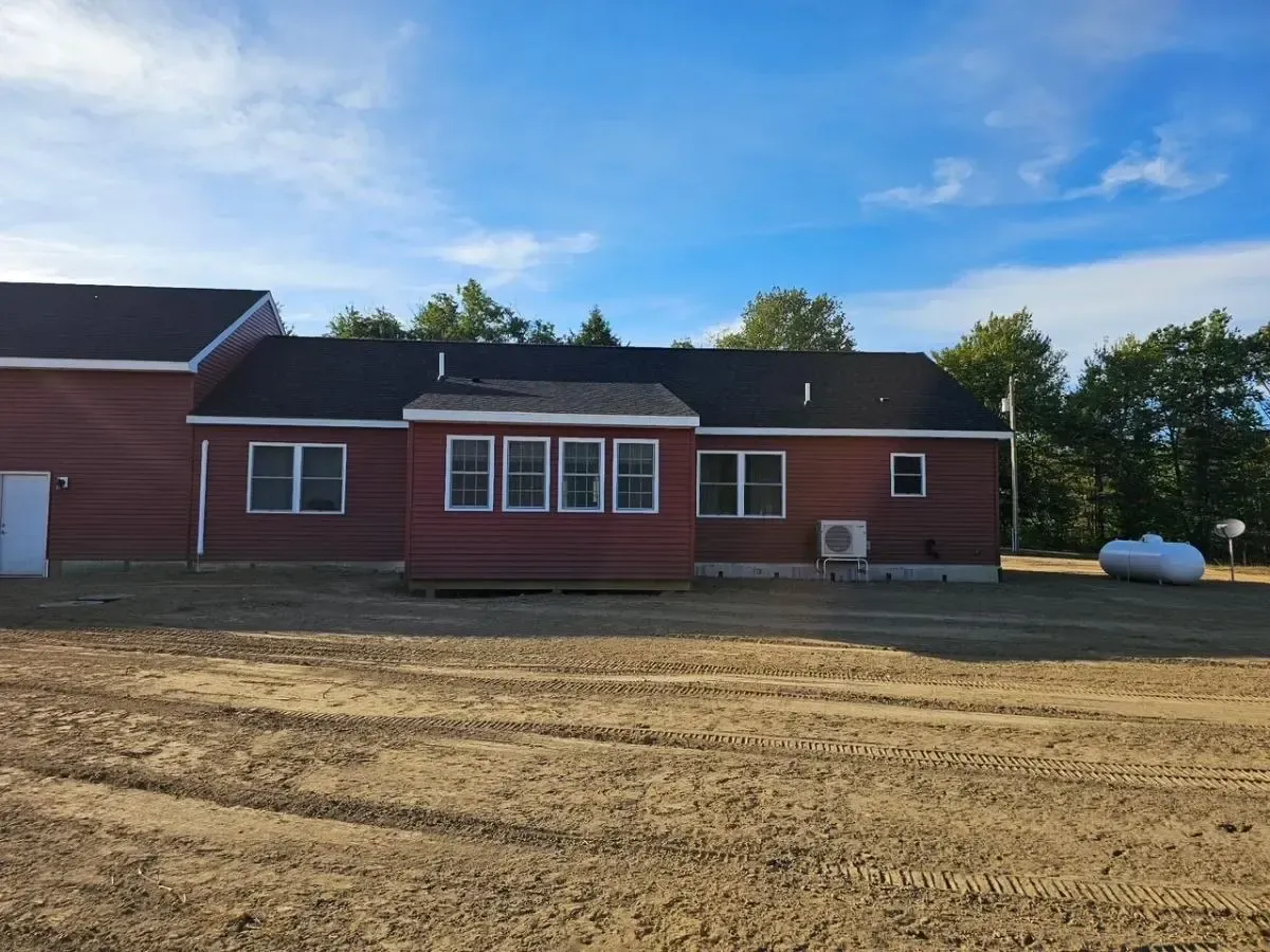 Red house with black roof, five windows, and a tank in front of a blue sky.