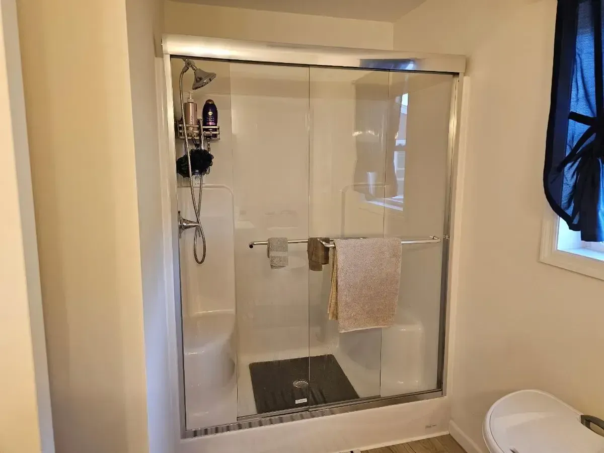 A glass-enclosed shower stall with white walls, built-in corner seats, a metal shower fixture, and a towel on the handle.