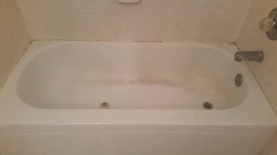 White bathtub with brown staining inside, surrounded by white tiles.