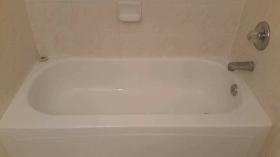 White bathtub in a bathroom with beige tile walls. Soap dish and faucet visible.
