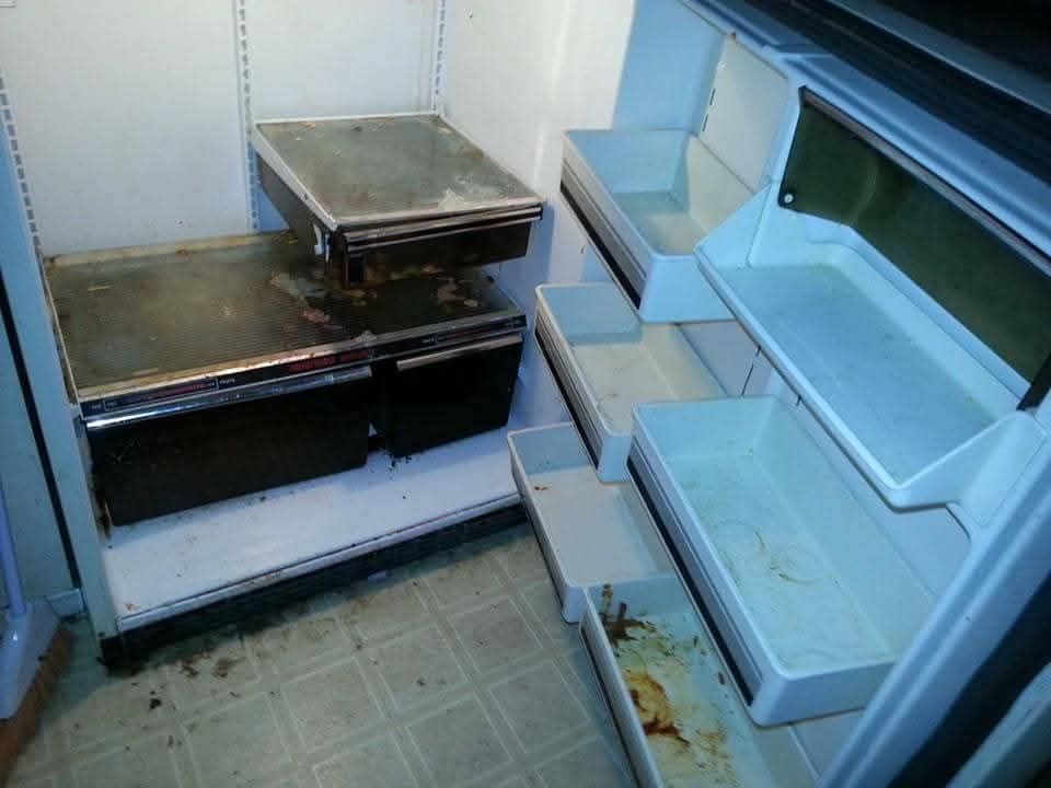 Empty, dirty refrigerator interior; shelves and drawers soiled with food and spills.